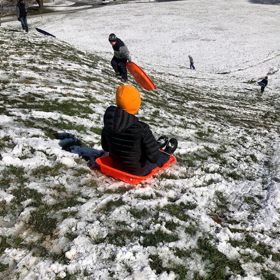 Person on a red sled on a snowy hill with other people in the background