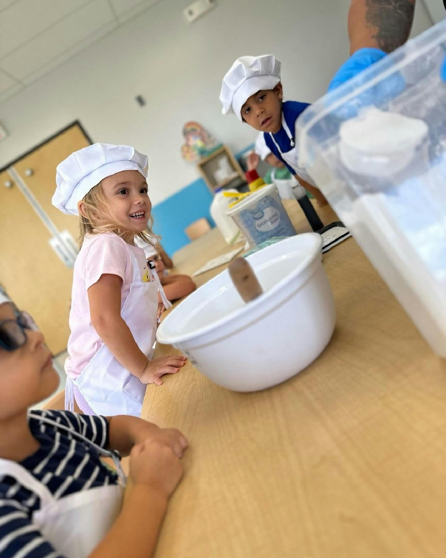 Children in chef hats and aprons at a table with a mixing bowl