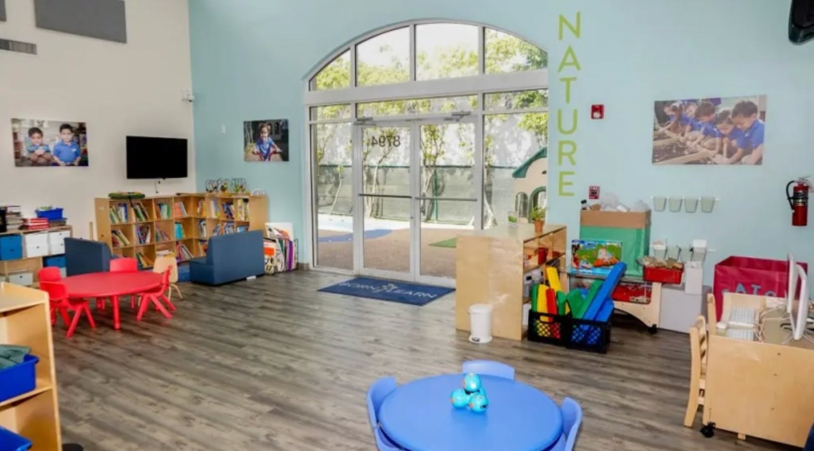 Empty classroom with small tables and chairs, bookshelves, and large glass doors