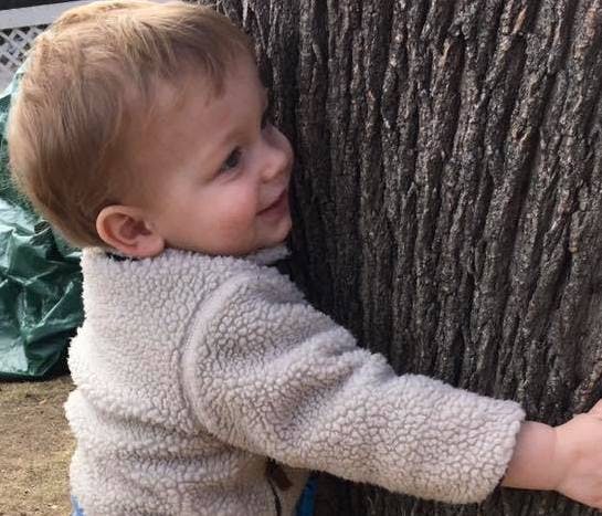 Child in a fleece jacket hugging a tree