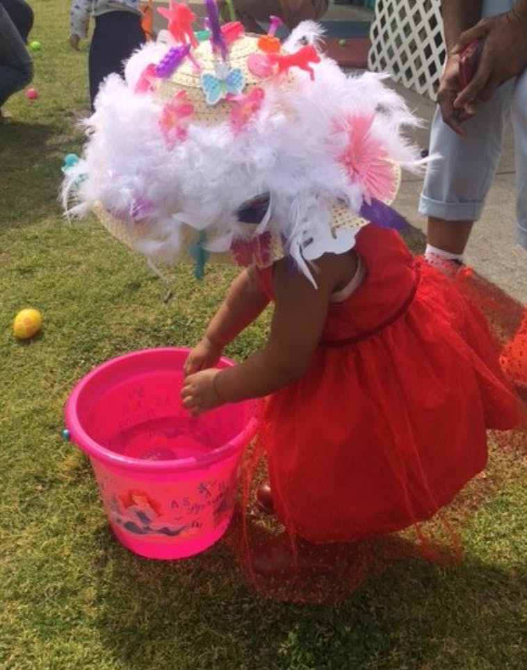 Child in a large decorative hat playing with a pink bucket