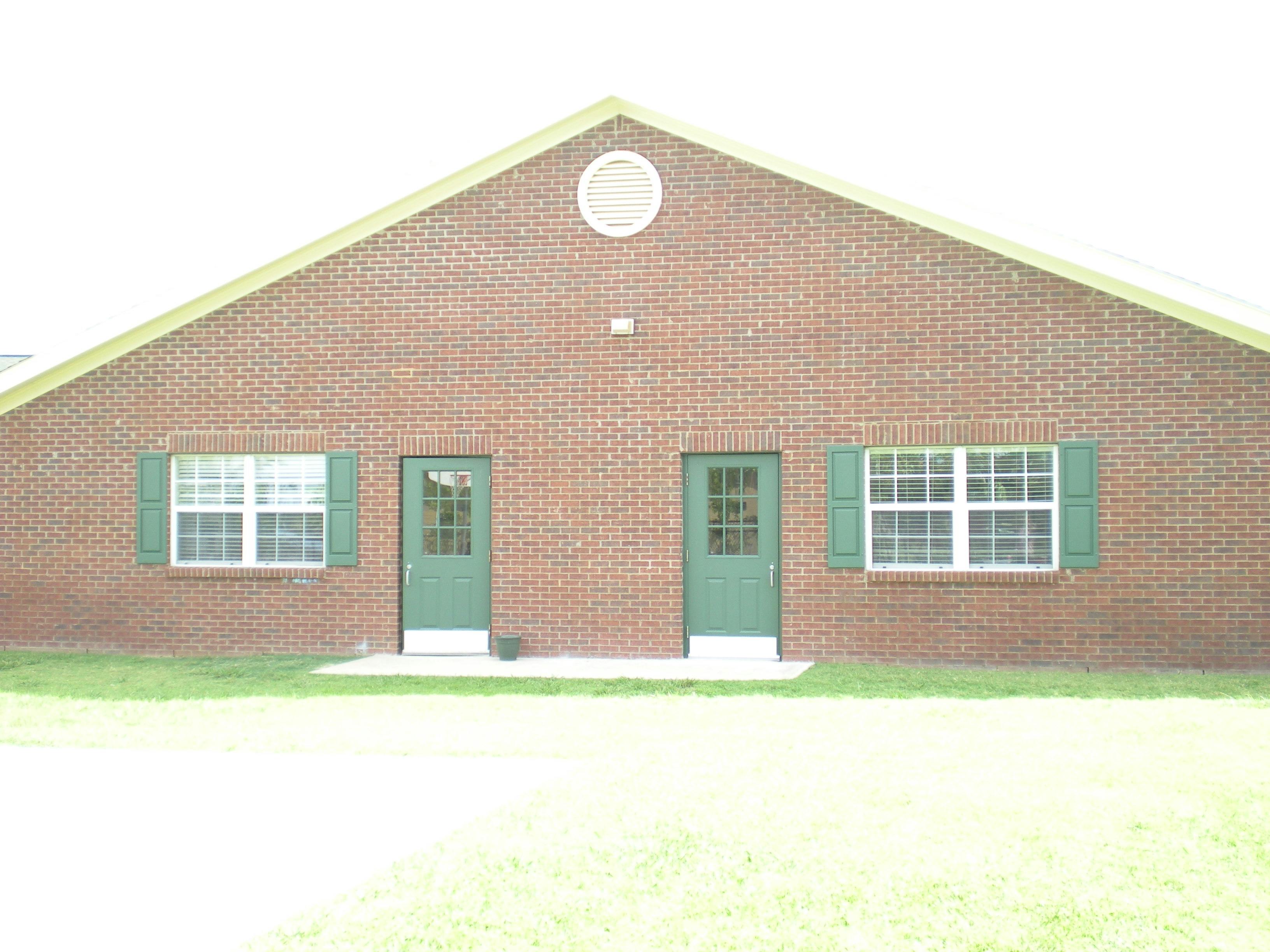 Brick building with two green doors and two windows with green shutters