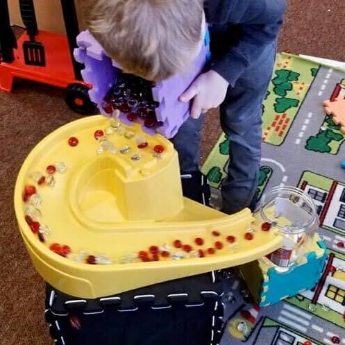 Child pouring small objects from a purple container onto a yellow toy