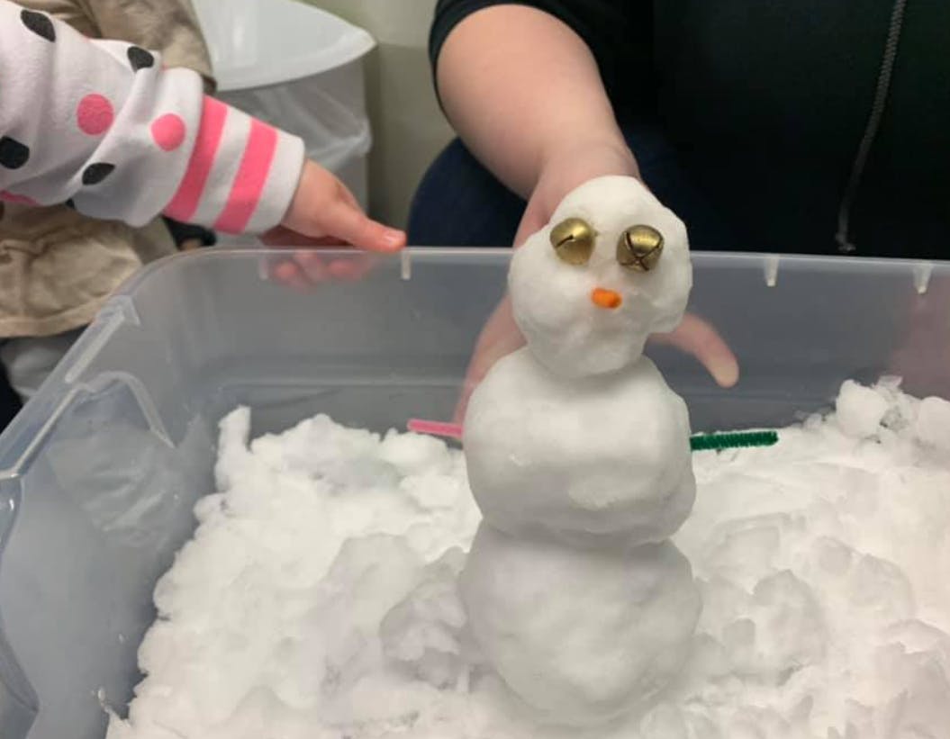 Person holding a small snowman with a child's hand nearby