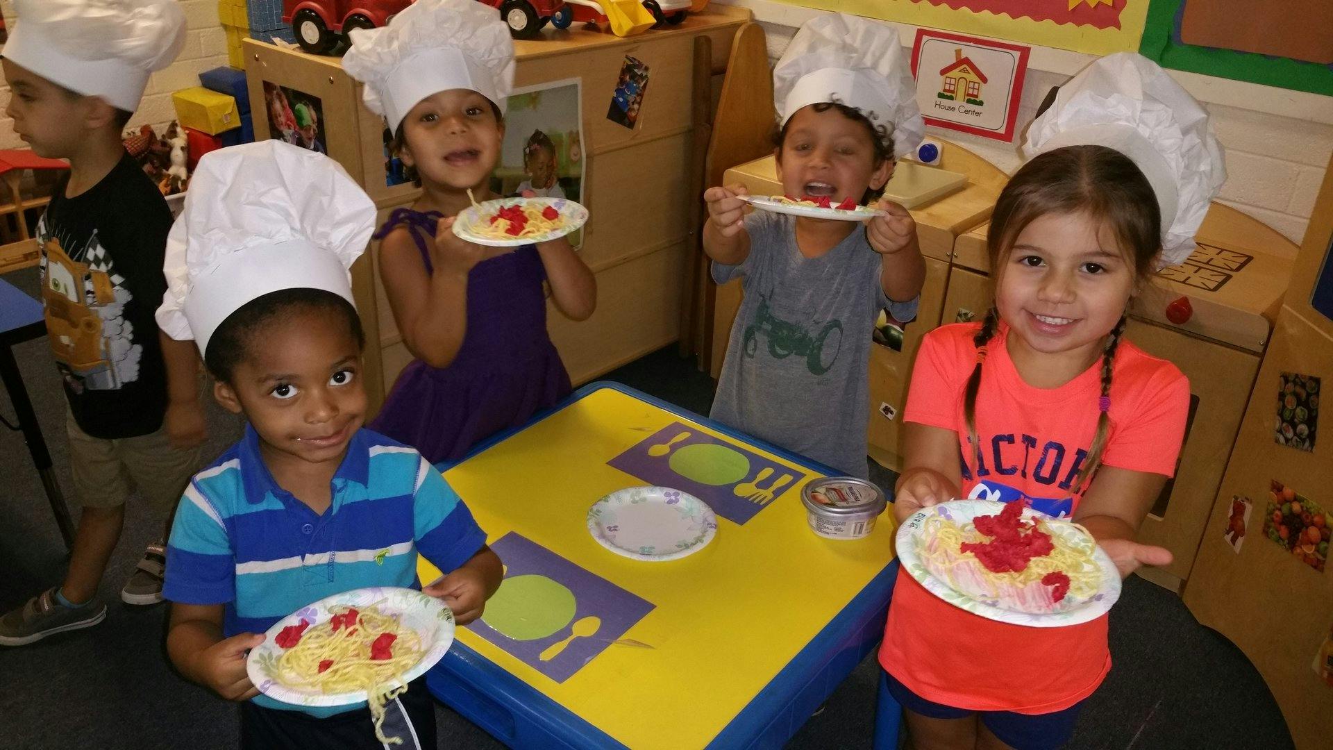 Four children in chef hats holding plates of food