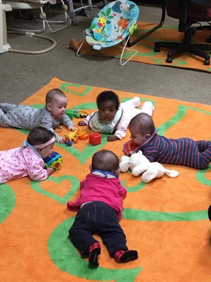 Five babies playing with toys on a colorful mat