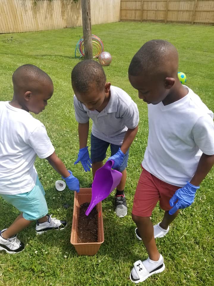 Three children wearing gloves, one pouring soil into a planter