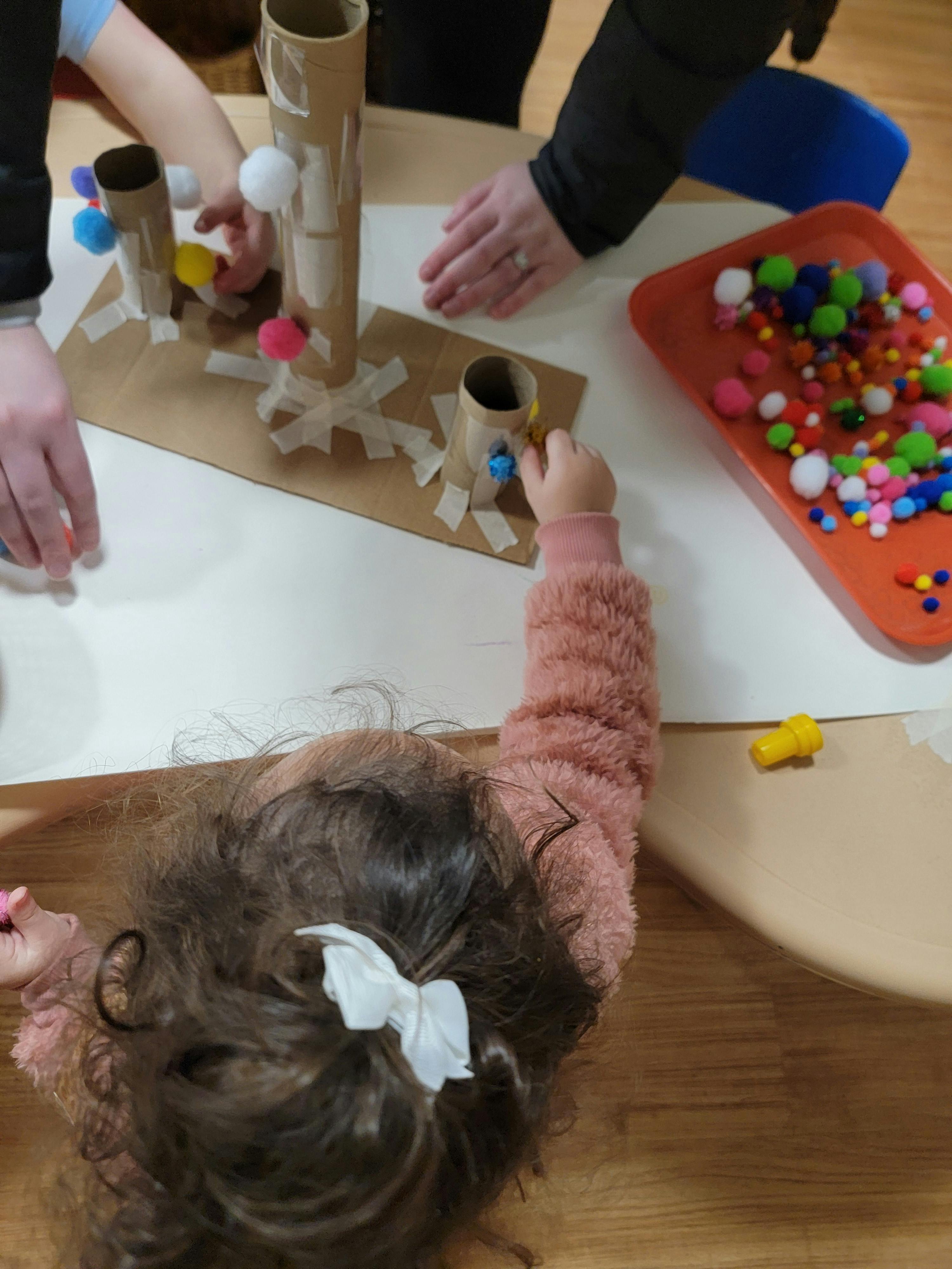 Child and adult making a pom-pom run with cardboard tubes and tape
