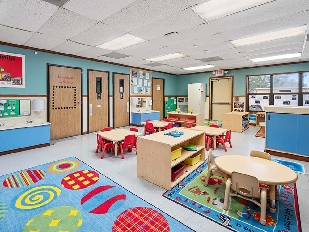 Colorful classroom with small tables and chairs, and play mats on the floor