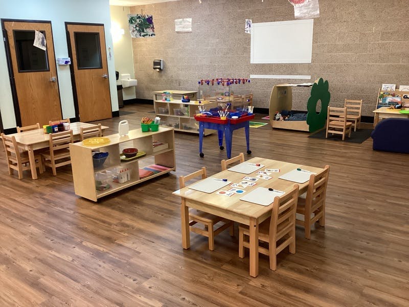 Classroom with child-sized tables and chairs, shelves with toys, and activity stations
