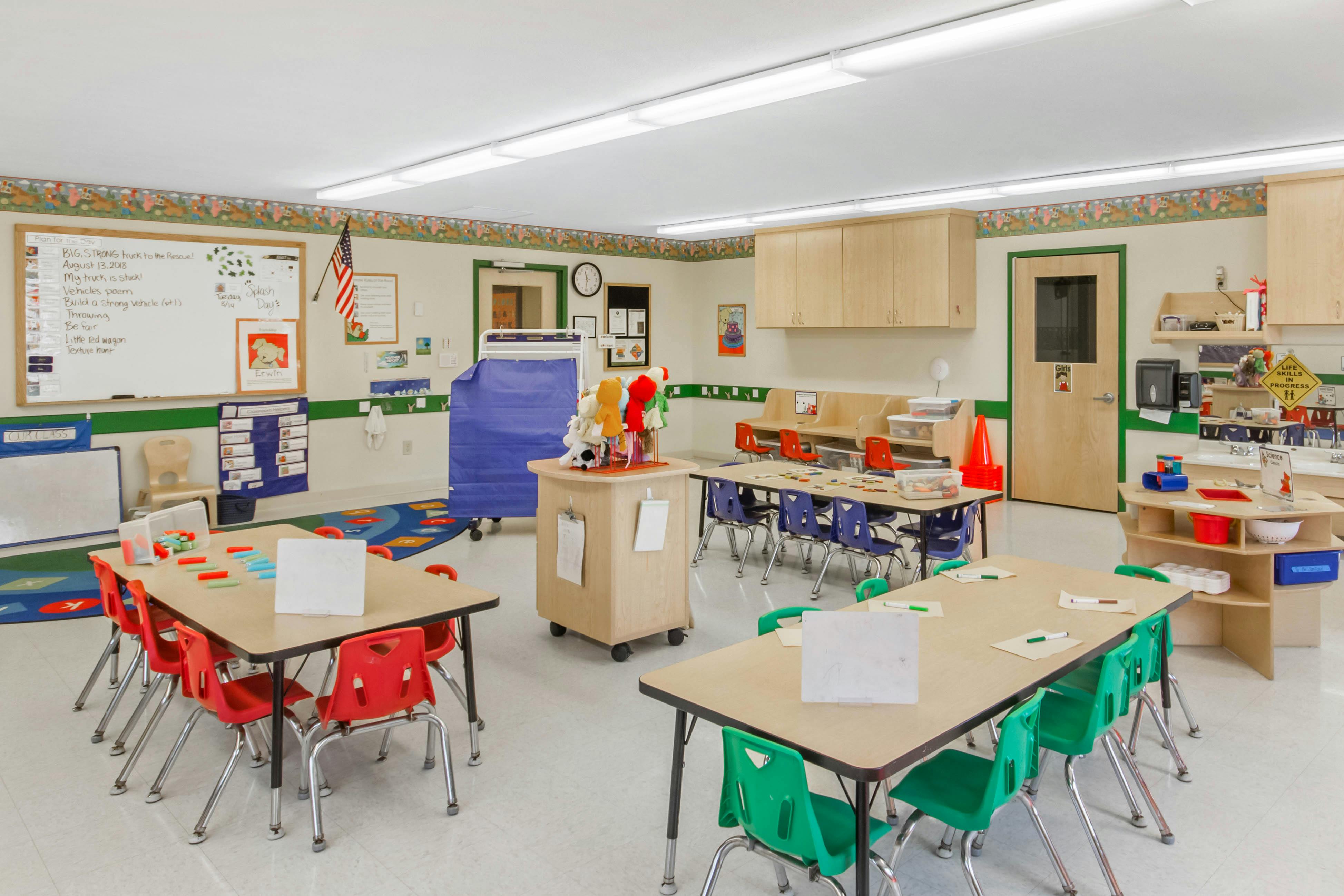 Classroom with multiple tables and chairs, whiteboard, and various learning materials