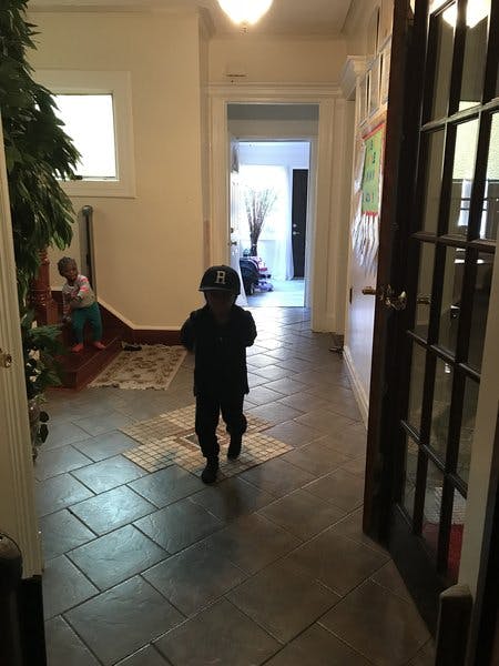 Child in a hat walking down a hallway, another child on stairs in the background