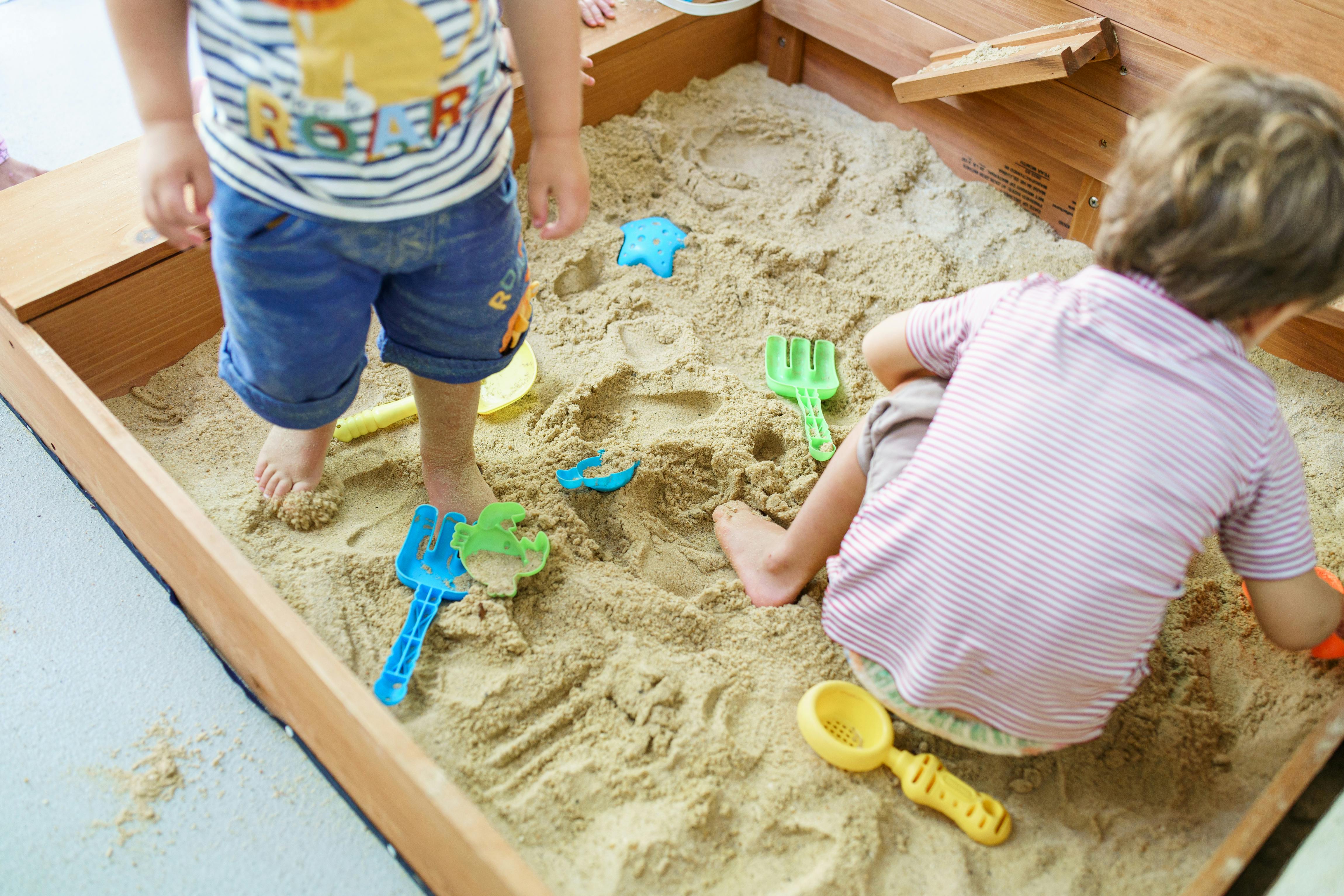 Two children playing in a sandbox with sand toys