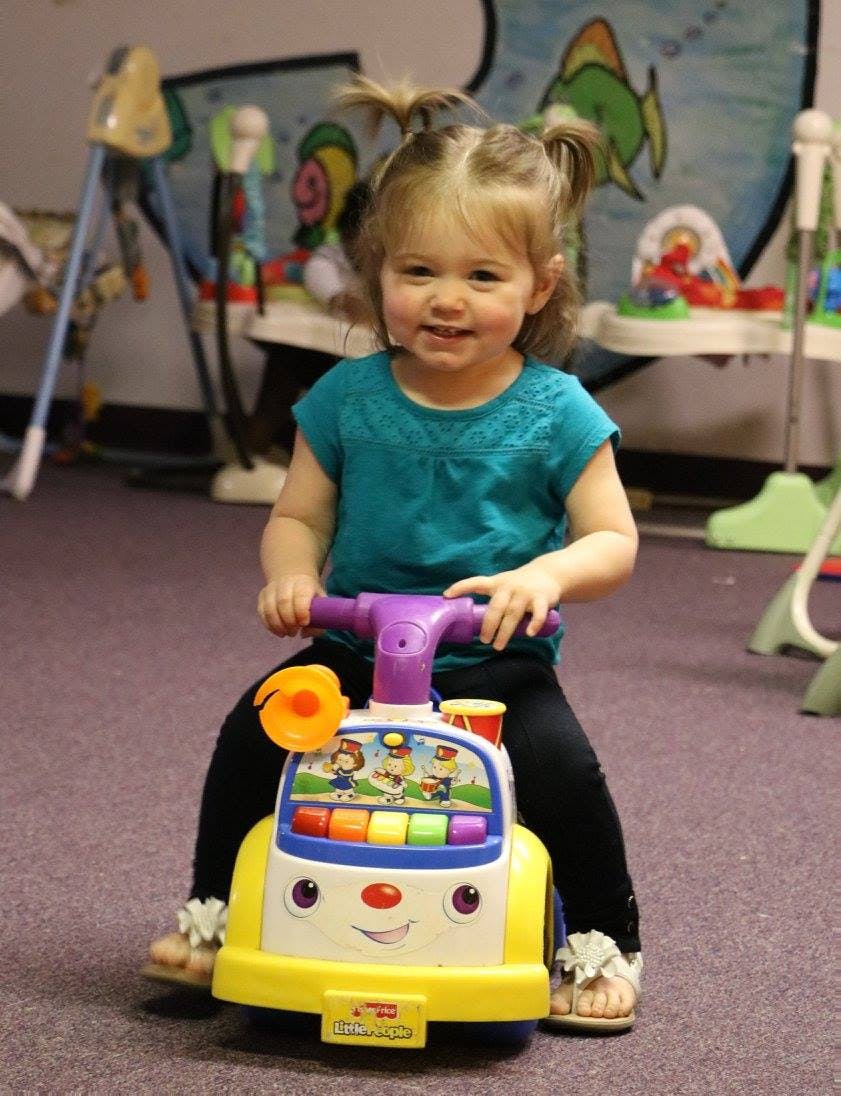 Child with pigtails sitting on a toy ride-on bus