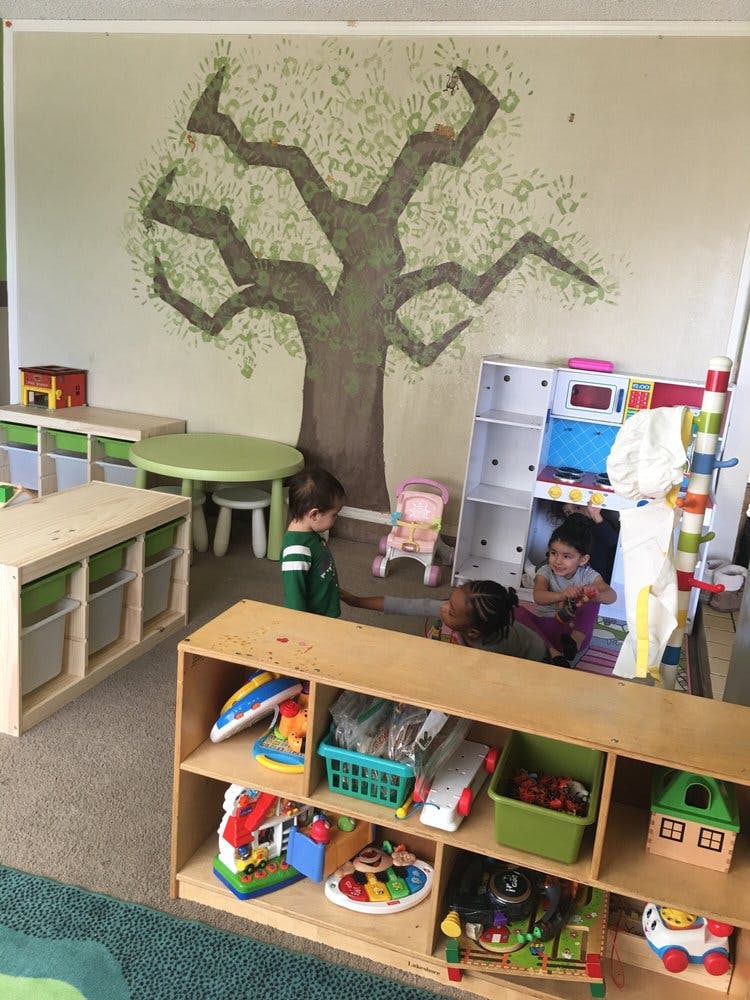 Children playing in a room with a tree mural and toy shelves