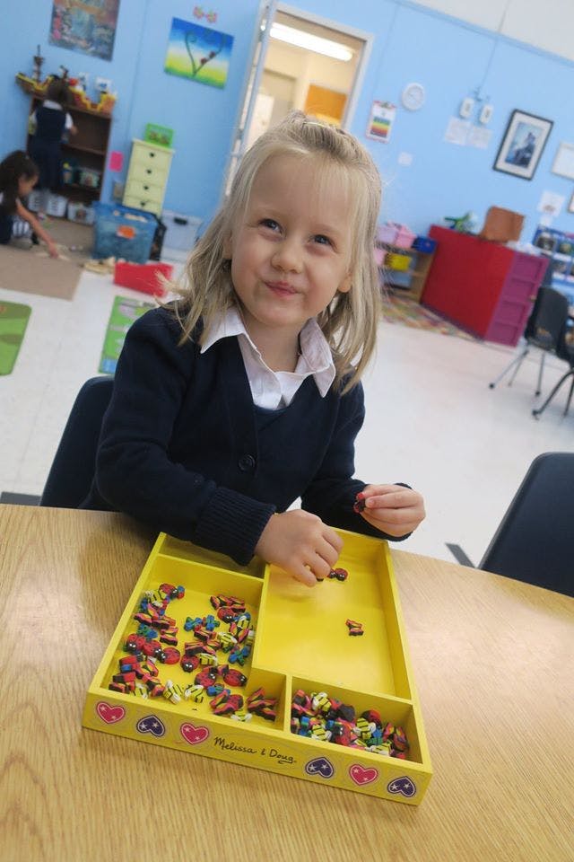 Child playing with small colorful pieces in a yellow tray