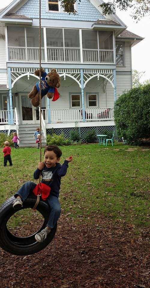 Child on a tire swing with a teddy bear hanging from a rope