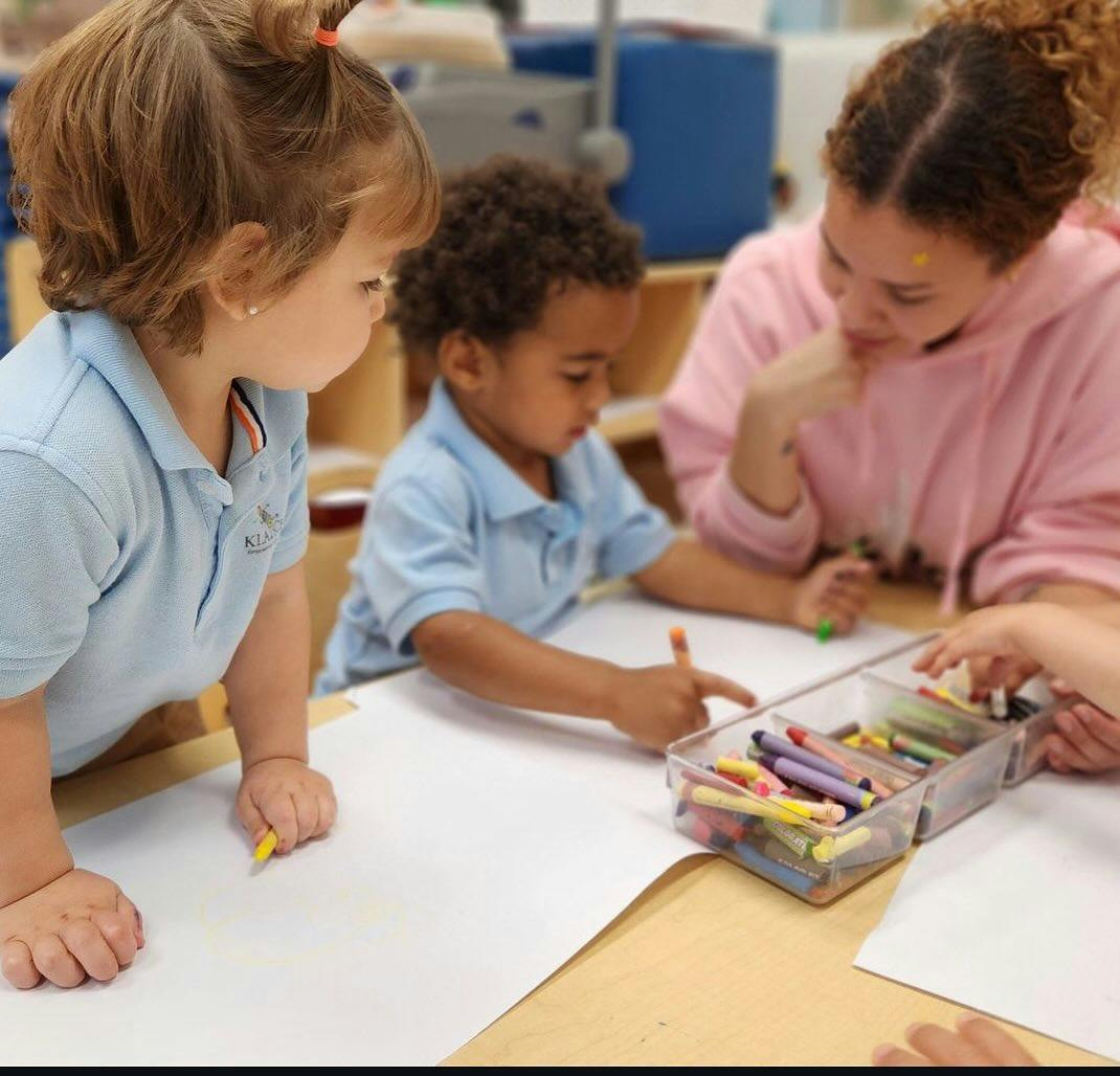Two children and a person drawing with crayons at a table