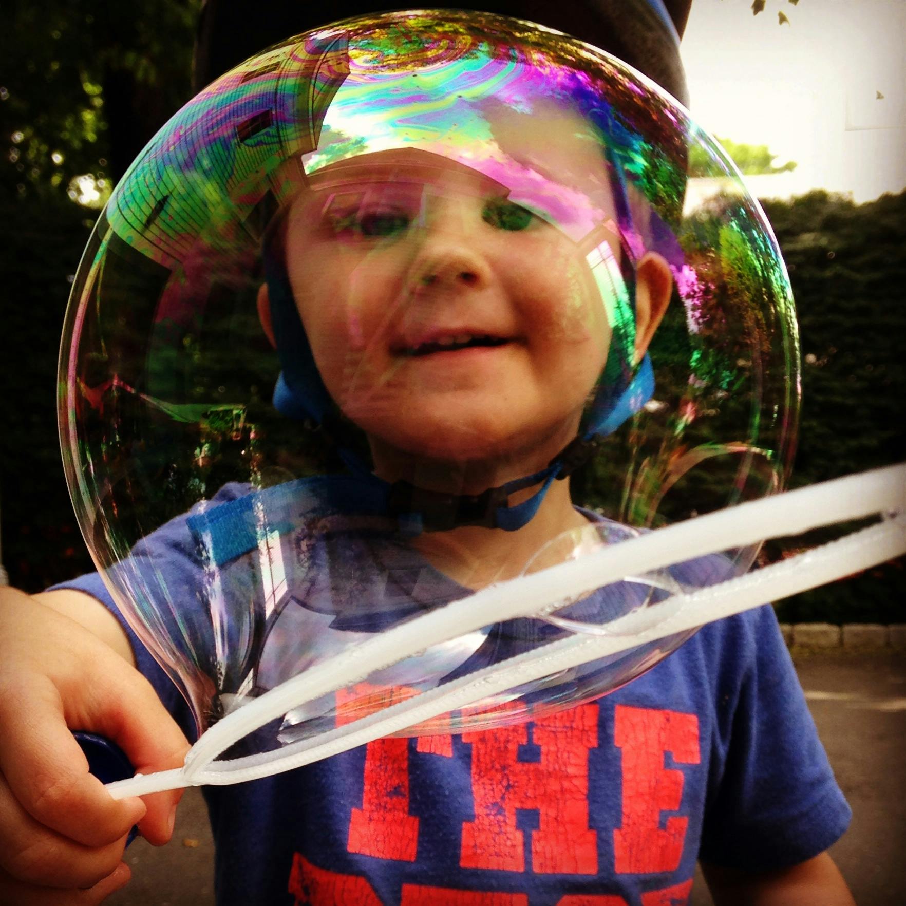 Child with a large bubble around their head, holding a bubble wand