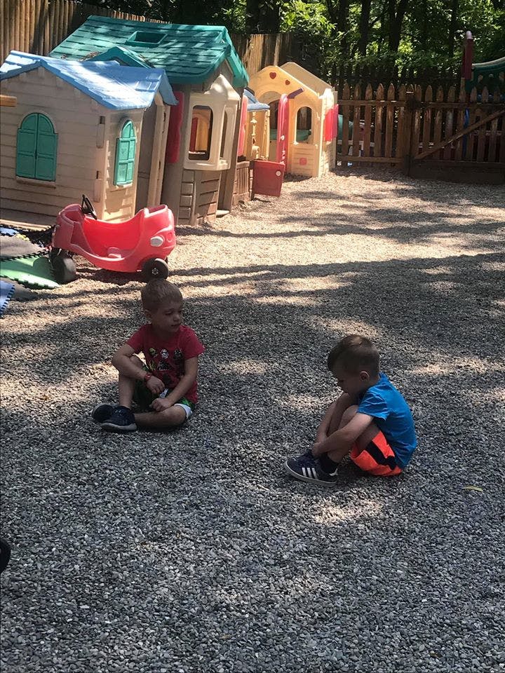 Two children sitting on gravel in a playground with playhouses
