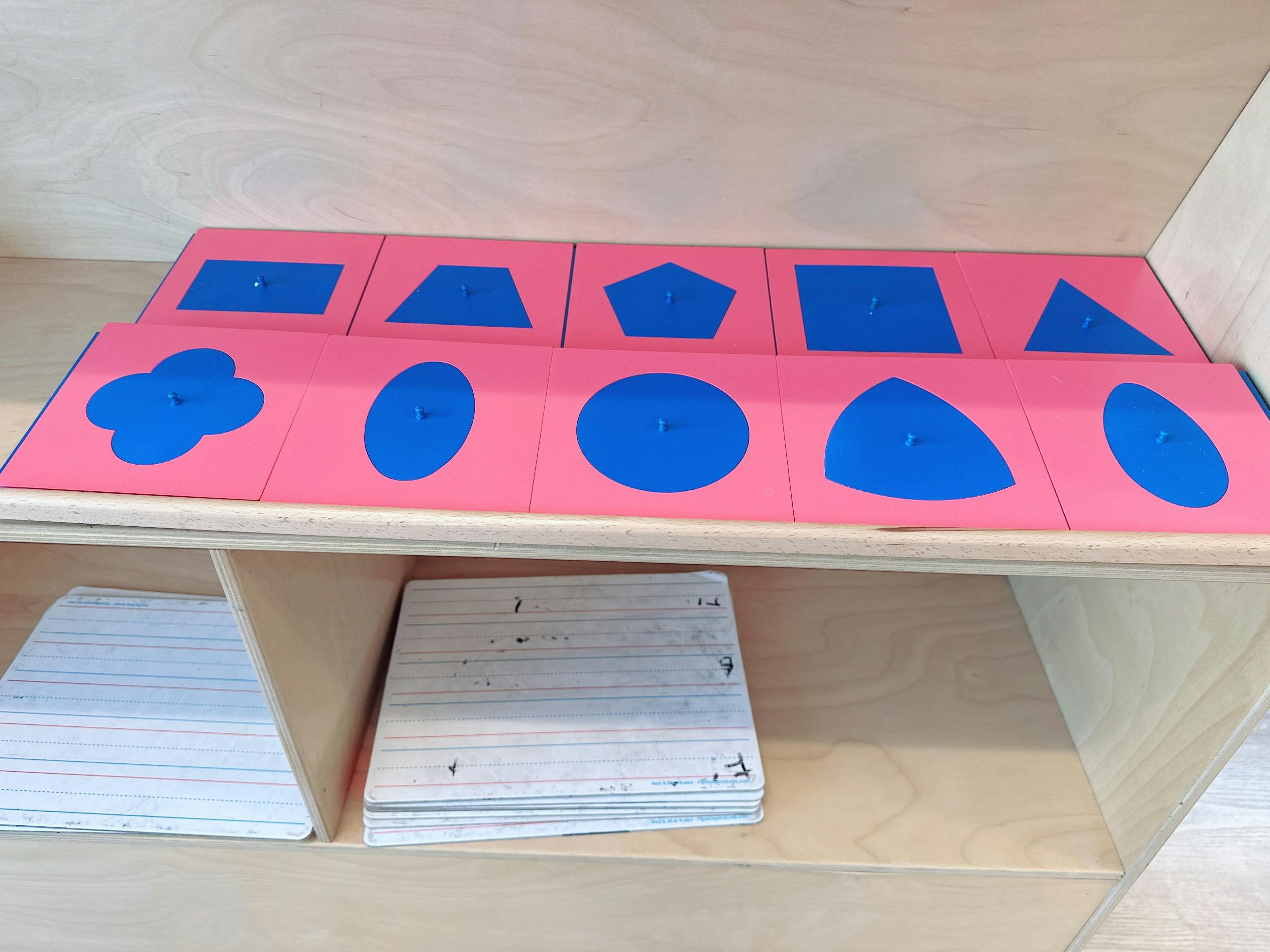 Set of blue geometric shapes on pink square tiles arranged on a wooden shelf