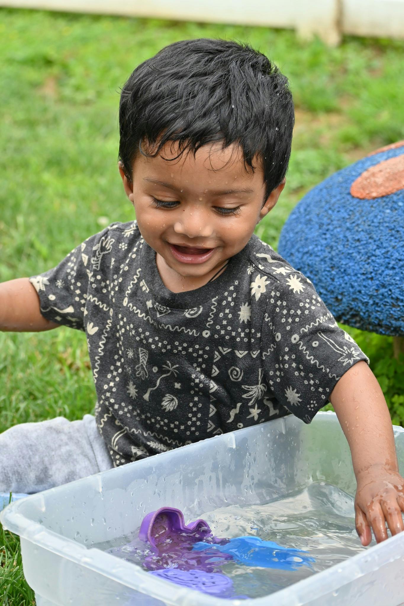 Child playing with water in a plastic bin with purple toys