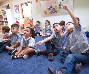 Children sitting on a blue carpet, looking up and pointing