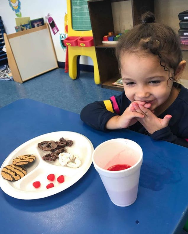 Child at a table with a plate of snacks and a cup