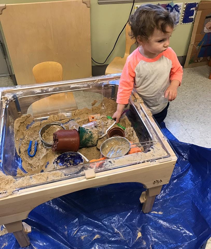 Child playing in a sand table with various containers