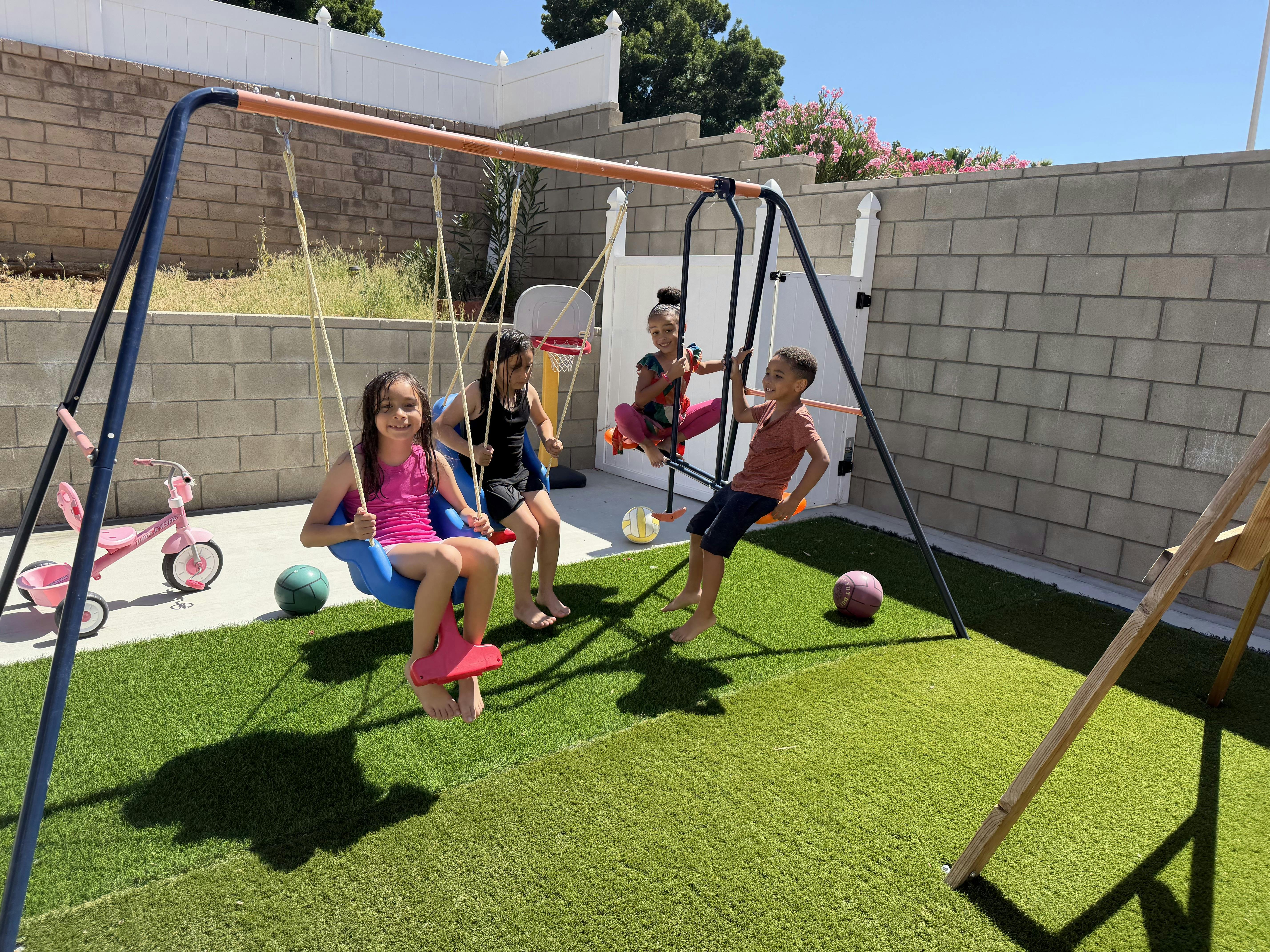 Four children playing on a swing set in a backyard