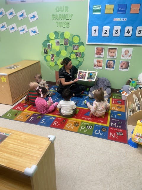 Person reading a book to several children sitting on a rug