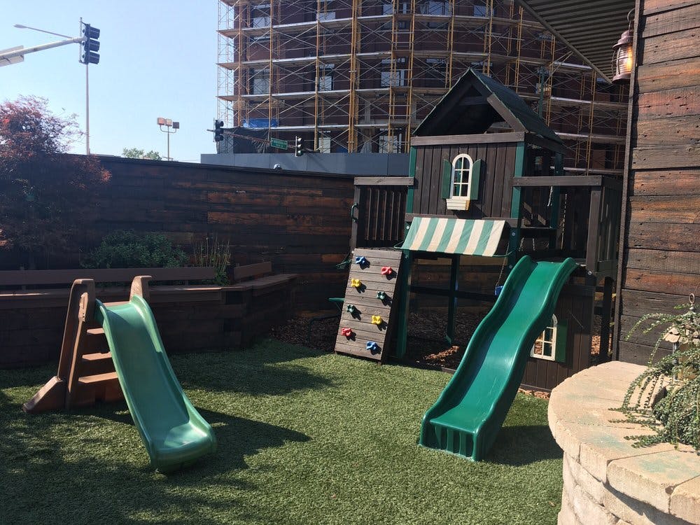 Two green slides and a playhouse with a climbing wall on artificial grass