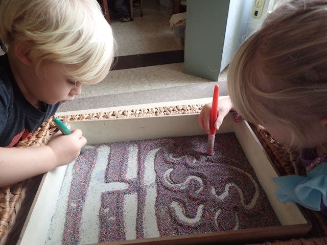 Two children drawing in a sand tray