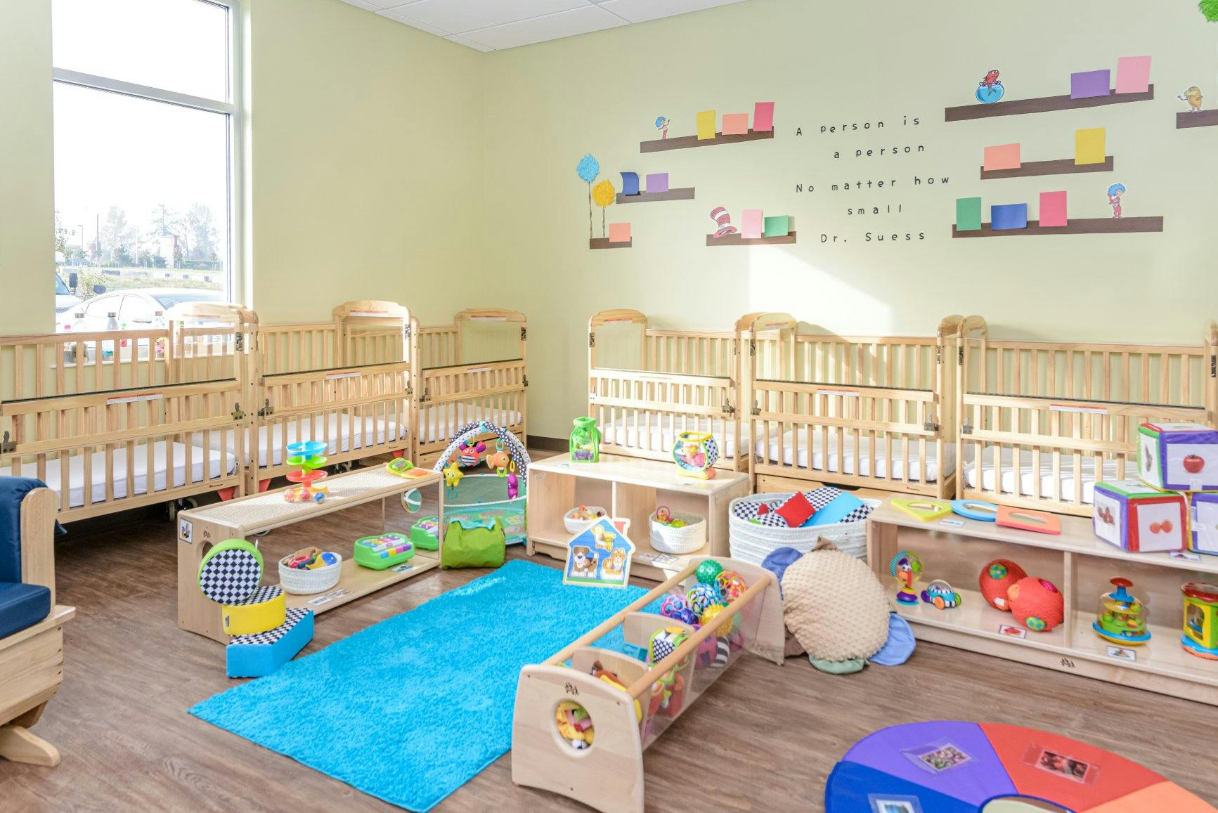 Cribs and toys in a childcare room with a large window