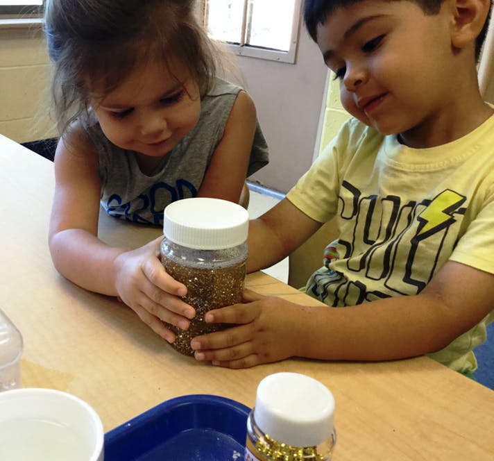 Two children looking at a jar filled with glitter