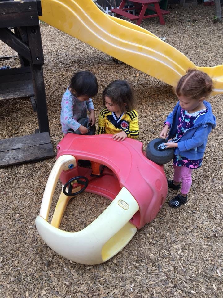 Three children playing with a toy car on a playground