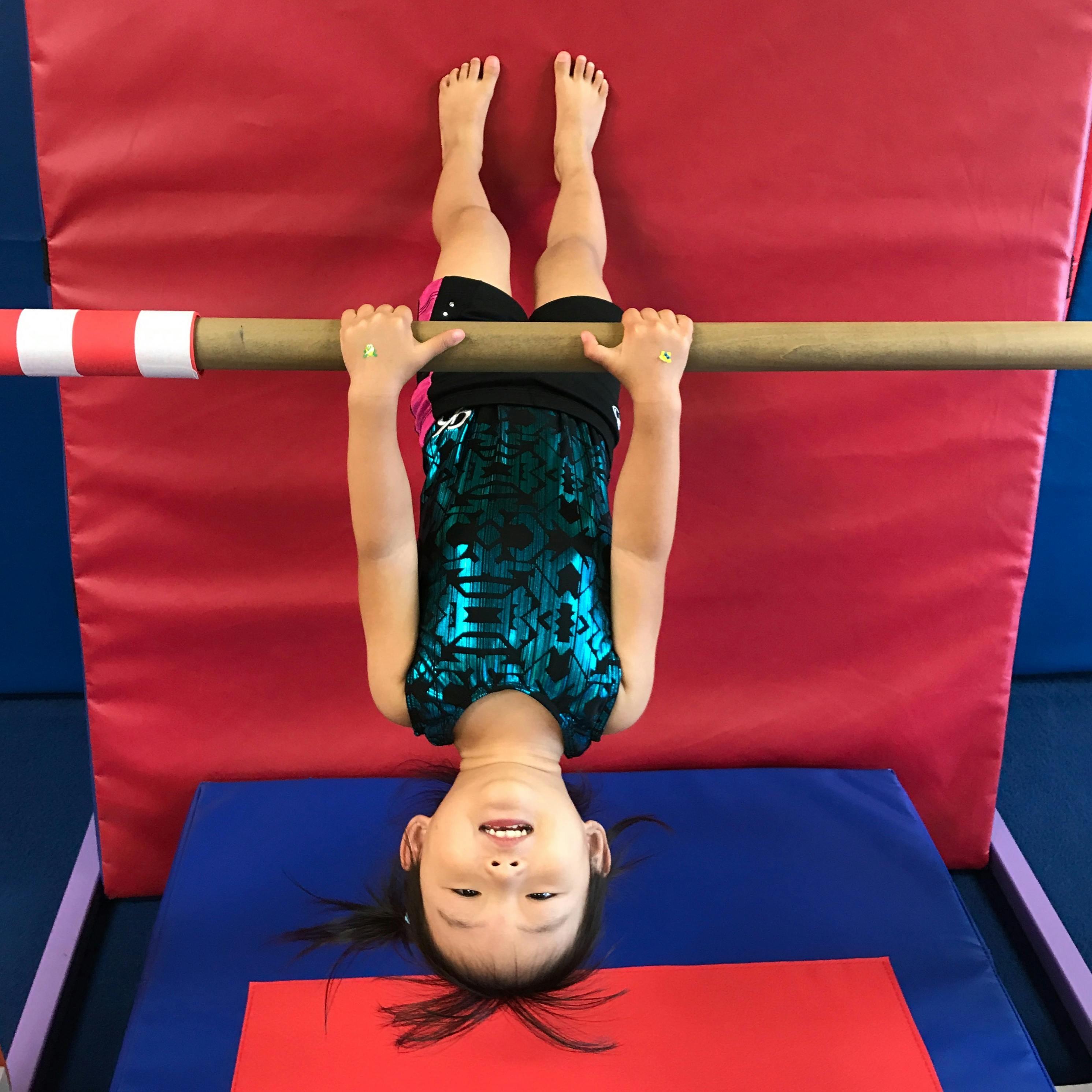 Child hanging upside down from a gymnastics bar