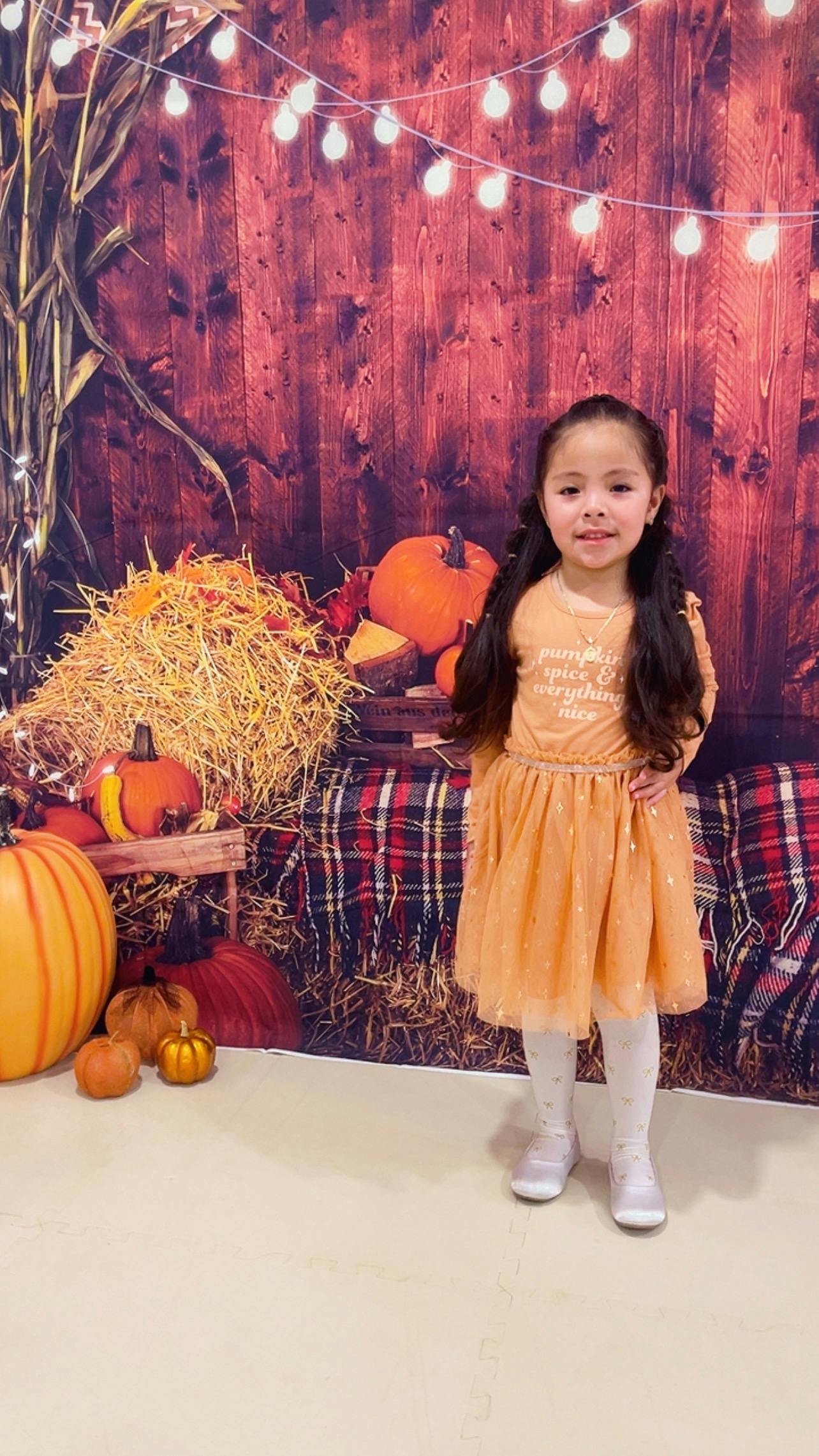 Child standing in front of hay bales and pumpkins