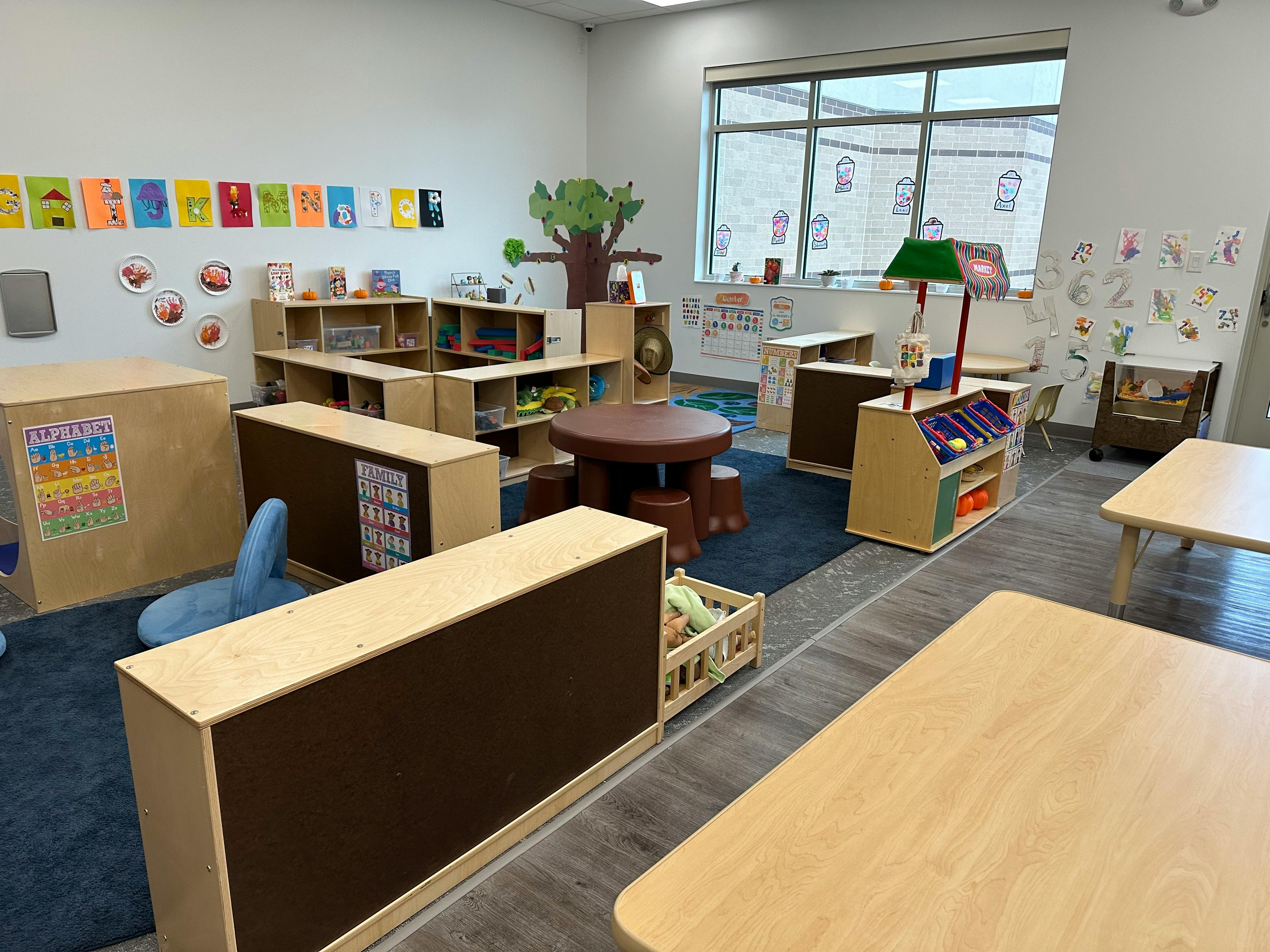 Empty classroom with small tables, chairs, and shelves