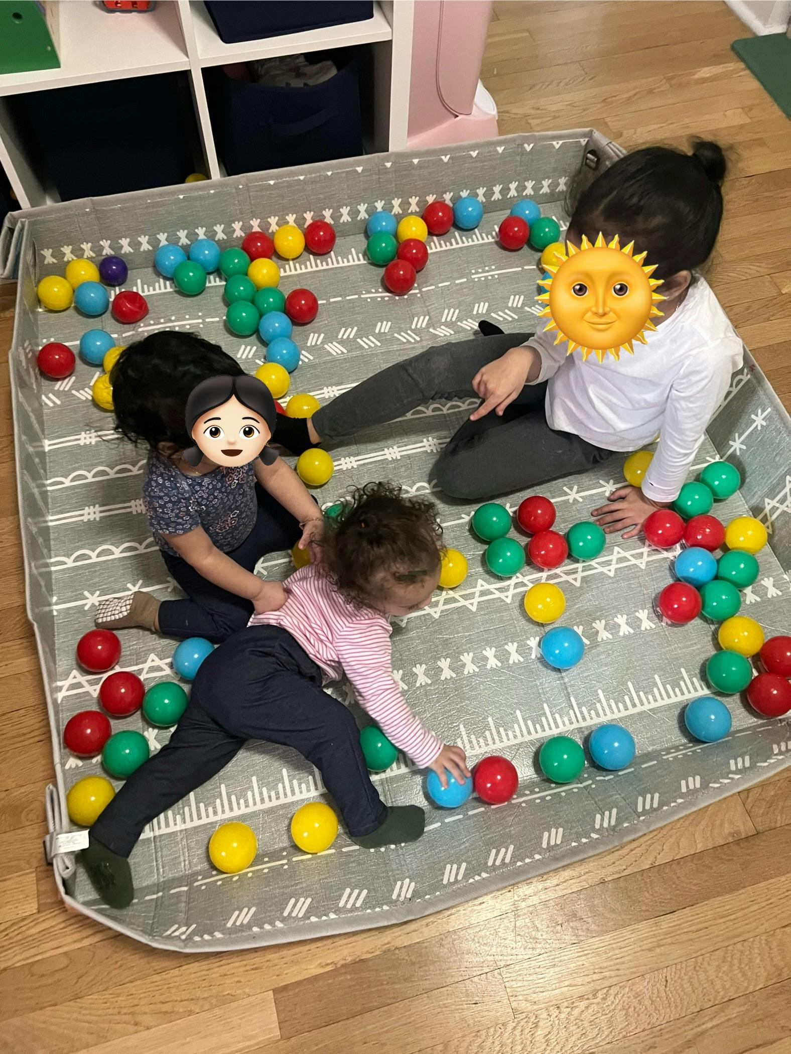 Three children playing with colorful balls in a soft playpen