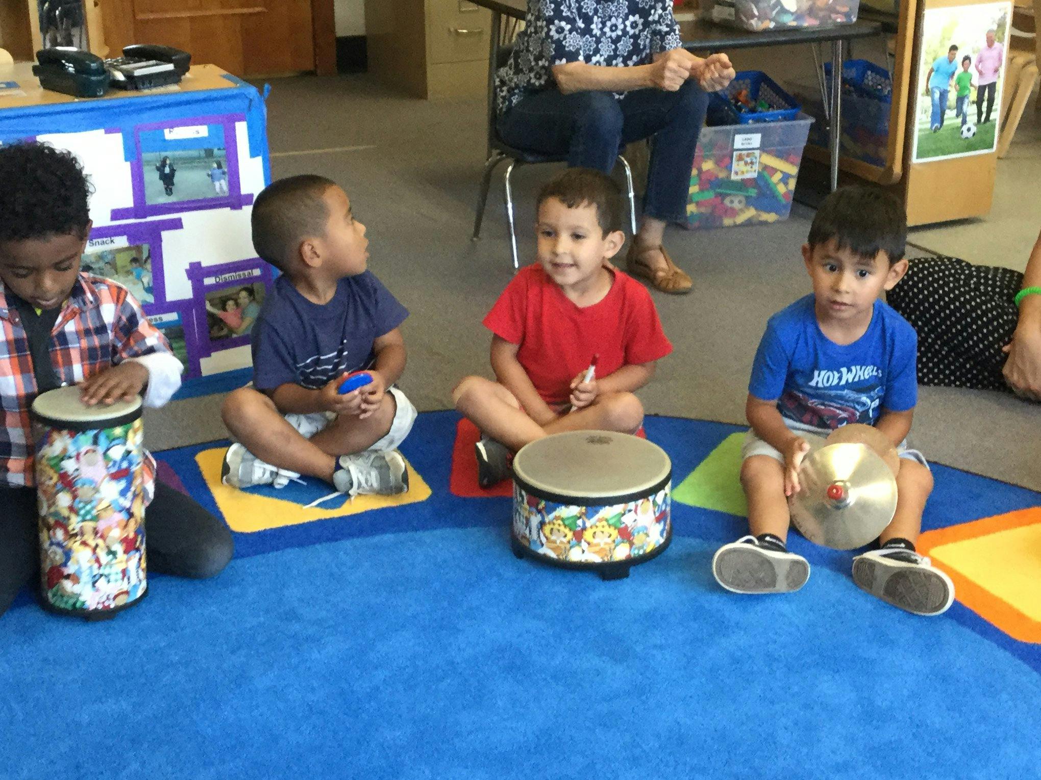 Four children sitting on a blue mat with musical instruments