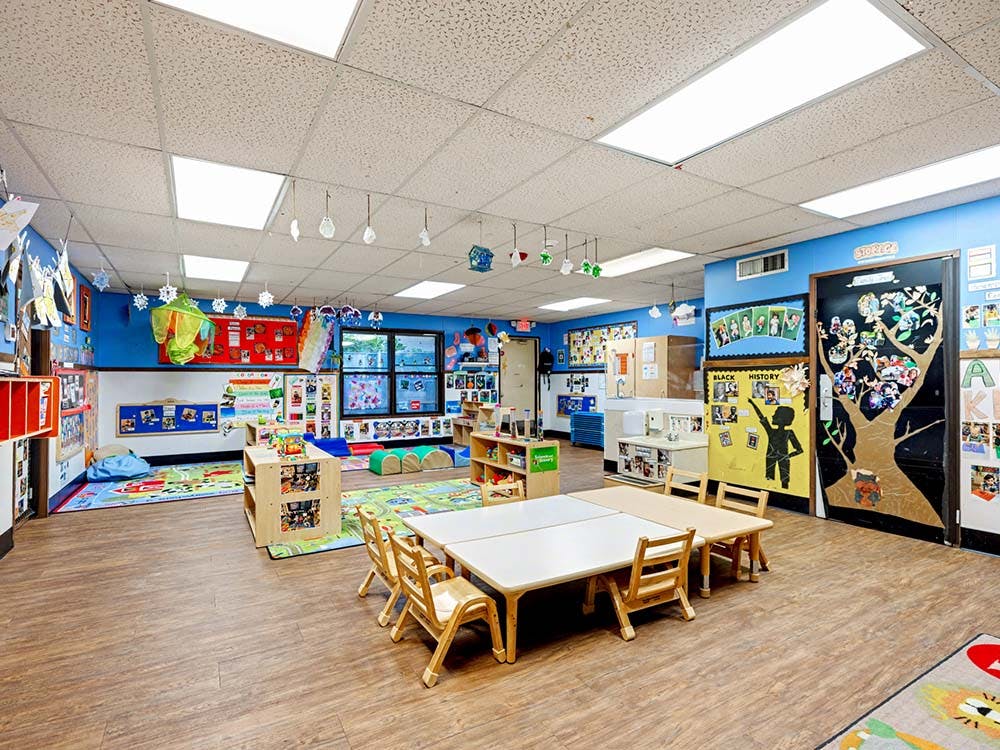 Empty classroom with small tables and chairs, colorful rugs, and decorated walls
