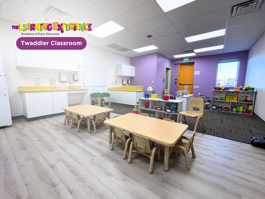 Classroom with small tables and chairs, shelves with toys, and a counter with a sink