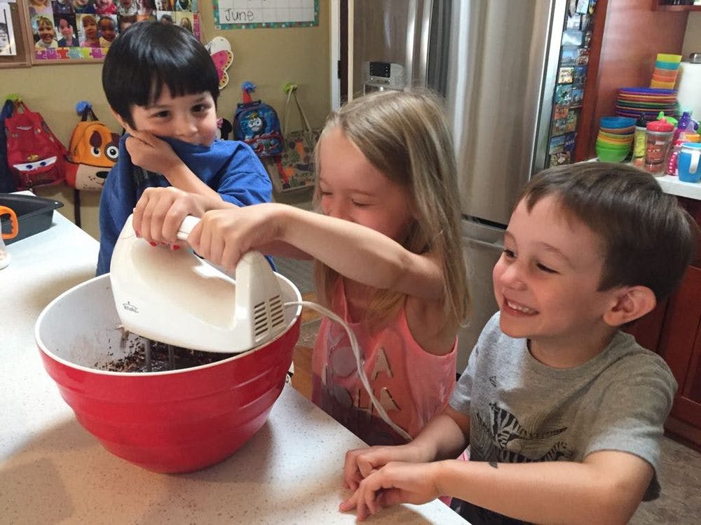 Three children mixing ingredients in a red bowl with a hand mixer