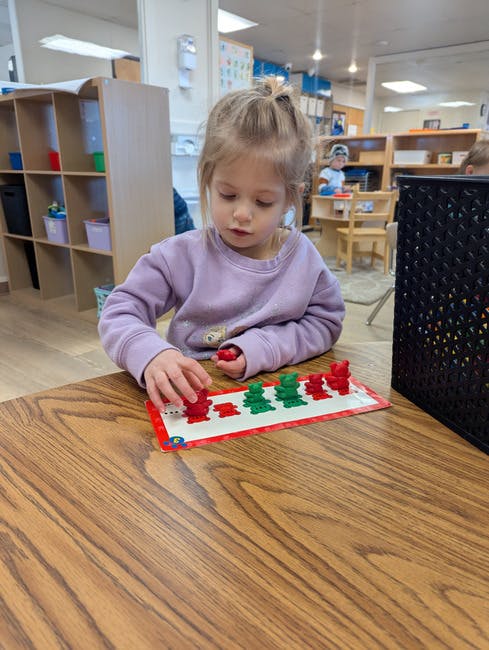 Child playing with red and green bear counters on a wooden table