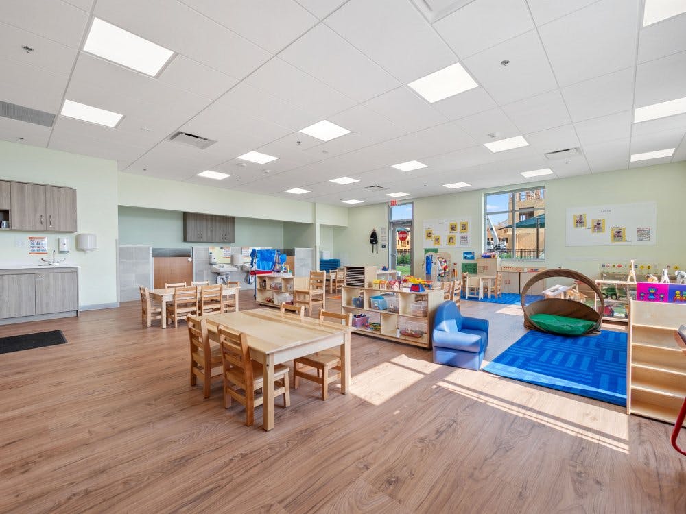 An empty children's classroom with small tables and chairs, and a play area