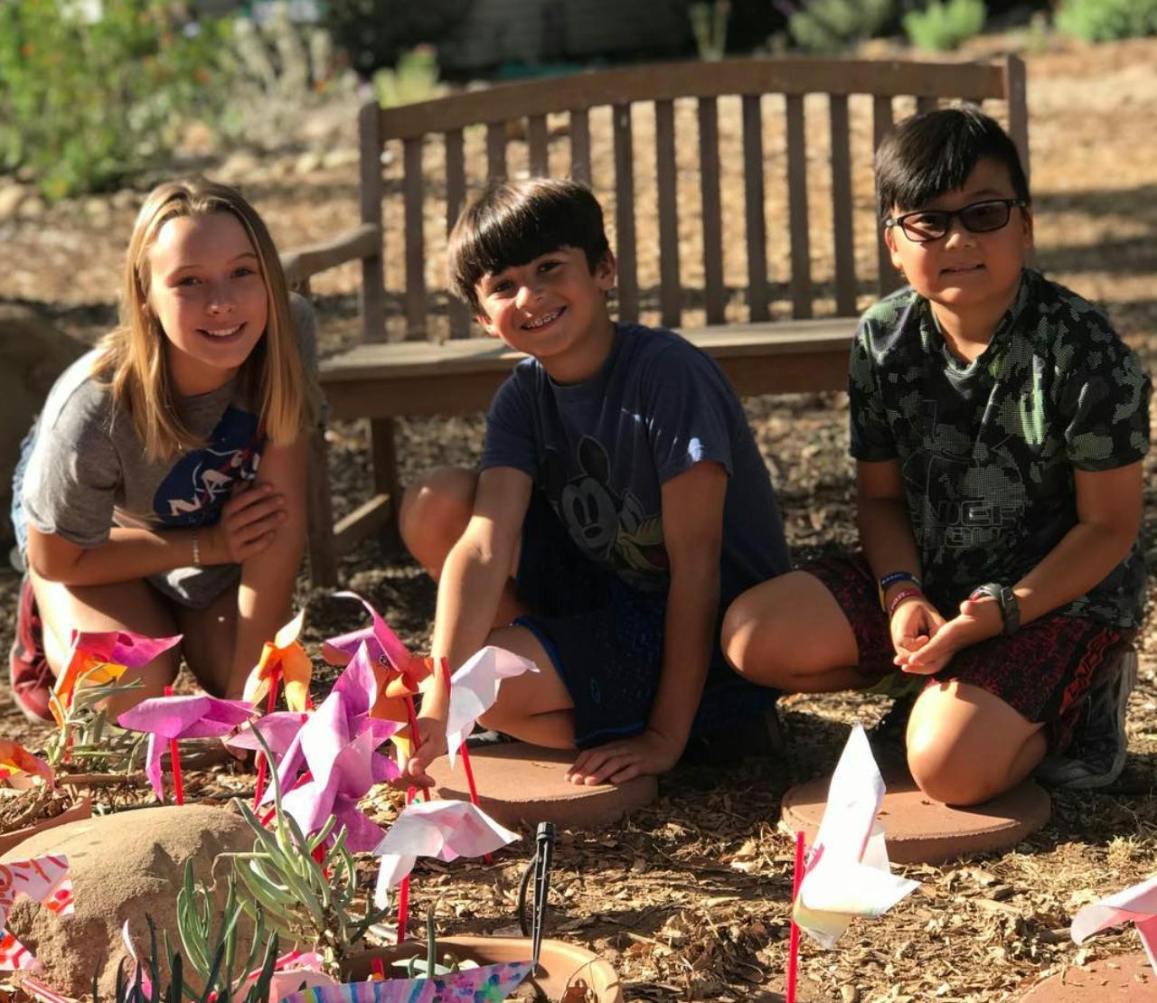 Three children crouching around paper crafts outdoors