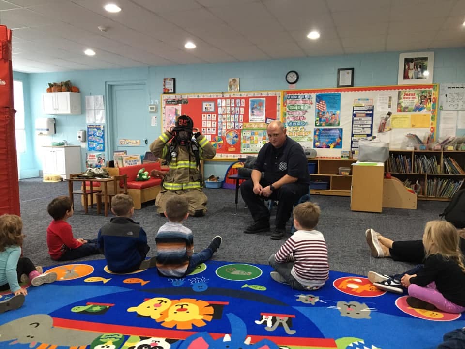 Firefighter in uniform and another person speaking to children in a classroom