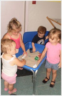 Four children playing with sand in a blue bin