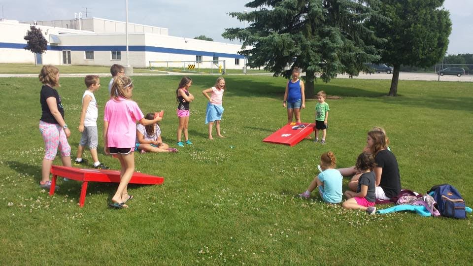 Children playing cornhole on a grassy field
